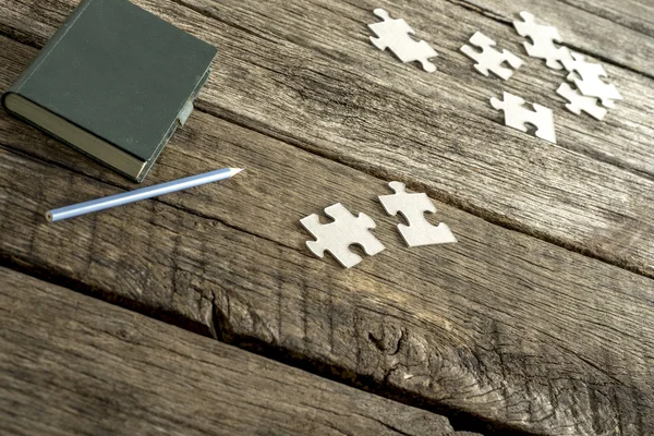 Grüner Notizblock, Bleistift und verstreute Puzzleteile liegen auf einem Tisch — Stockfoto