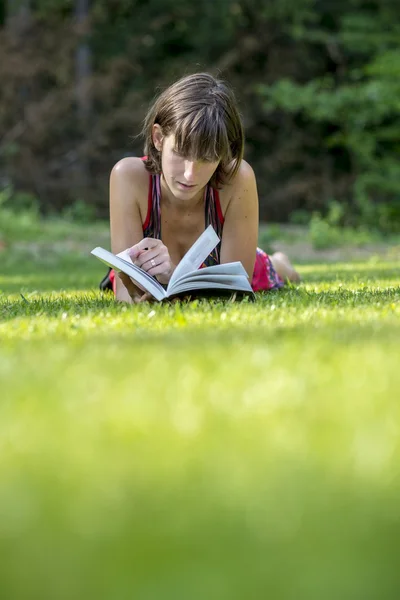 Young woman lying in green grass reading a book — Stock Photo, Image