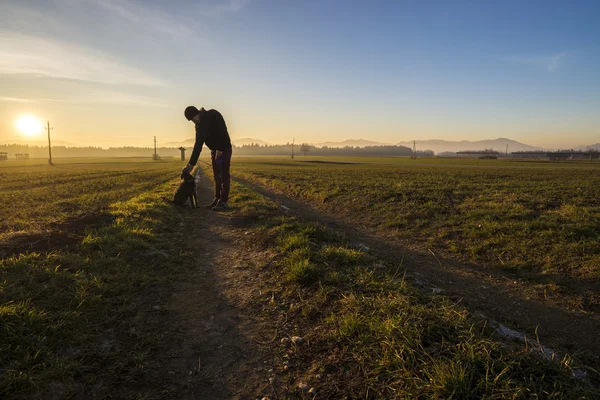 Uomo in piedi su una strada di campagna appoggiata al suo cane nero — Foto Stock