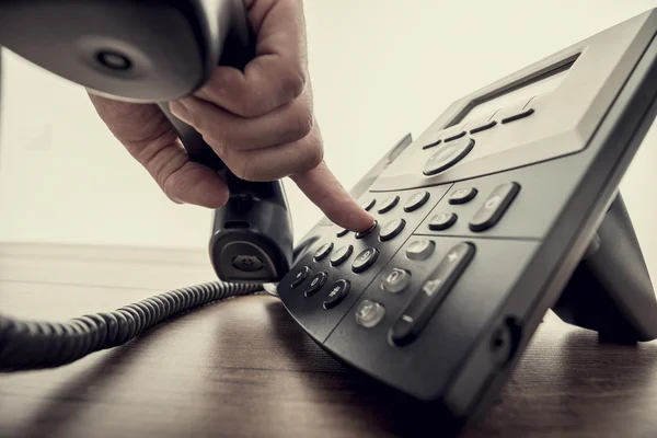 Male hand holding telephone receiver and dialing a phone number