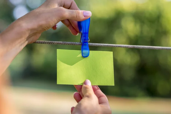 Female hand hanging a blank green card with plastic peg — Stock Photo, Image