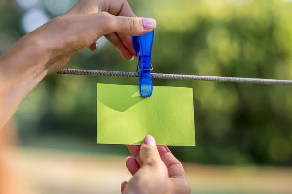 Main féminine accrochant une carte verte vierge avec une cheville en plastique — Photo