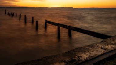 Turuncu gün batımı. Baltık Denizi 'ndeki eski iskelenin parçalanmış ahşap yığınları ufku terk ediyor.