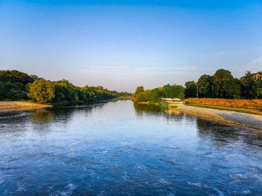 Güneşli bir sabahta ağaçların arasında dalgaların olduğu uzun bir nehir.