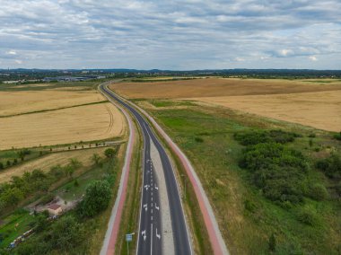 Bulutlu bir günde sarı buğday tarlaları arasındaki uzun otobanın havadan görünüşü