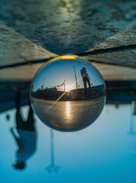 Man silhouette on skateboard reflected in crystal glassy lensball