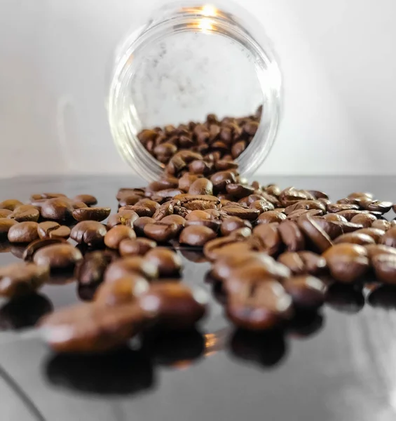 A lot of coffee beans lie on glassy surface fallen out of glassy vessel