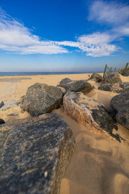 Büyük kayalar ve kumlu kum tepeleri Baltık Denizi kıyısında dağınık bulutlu mavi gökyüzünün altında
