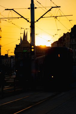 Wroclaw, Polonya - 17 Eylül 2024: Canlı altın bir gökyüzüne karşı hareketli bir tramvay istasyonunda, silüet binalar ve tramvay hatlarıyla nefes kesici bir gün batımı yakalandı