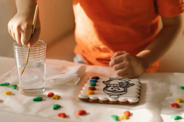 Seorang anak melukis kue jahe mengkilap dengan pewarna makanan. Kreativitas dan hobi — Stok Foto