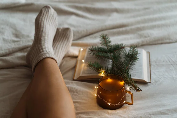 Woman is lying feet up on white shaggy blanket and reading book. Cozy leisure scene. Woman relaxing at home — Stock Photo, Image