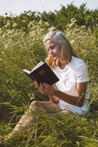 Adolescente cristiana leyendo la Biblia en el campo. Concepto de fe, espiritualidad y religión — Foto de Stock