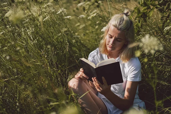 Tienermeisje die het boek in het veld leest. Het meisje dat op een gras zit en een boek leest.. — Stockfoto