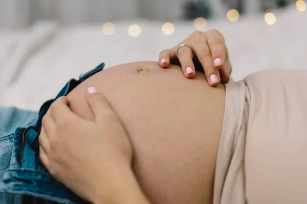 หญิงตั้งครรภ์ที่น่าสนใจนั่งอยู่บนเตียงและถือท้องของเธอ แนวคิดการตั้งครรภ์ . — ภาพถ่ายสต็อก