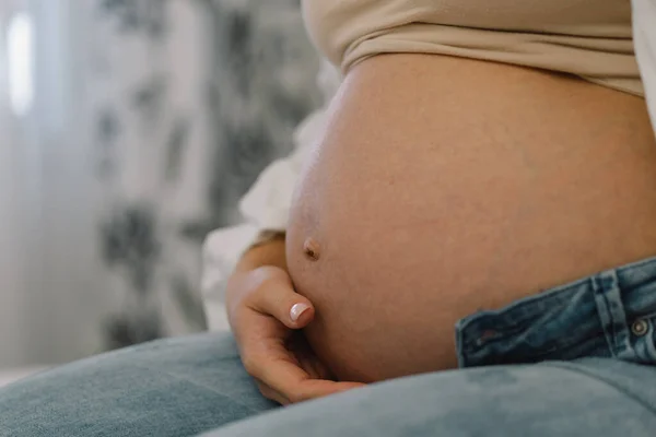 หญิงตั้งครรภ์ที่น่าสนใจนั่งอยู่บนเตียงและถือท้องของเธอ แนวคิดการตั้งครรภ์ . — ภาพถ่ายสต็อก