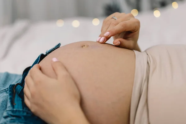 Atractiva mujer embarazada está sentada en la cama y sosteniendo su vientre. Concepto de embarazo. — Foto de Stock