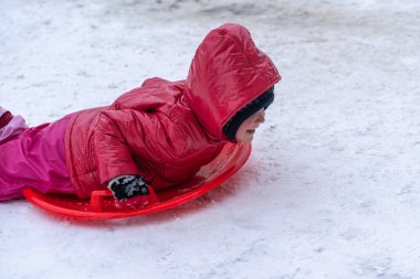 Küçük bir kız kış kaydırağından kızakla kayıyor. Kış tatili.