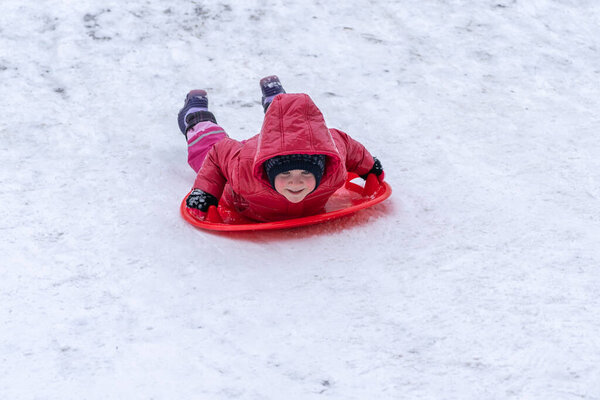 A little girl rides a sled from a winter slide. Winter holidays.