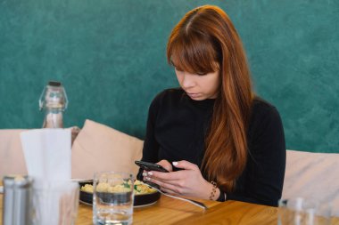 Güzel kız kafede yemek yerken cep telefonu kullanıyor.