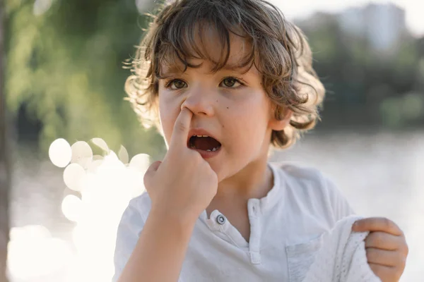 Cute boy picking one\'s nose in nature. Facial expressions and emotions.