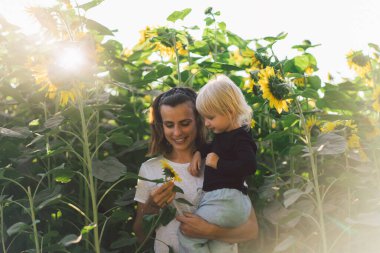 Genç anne bebeğini kucağında tutuyor. Anne ve küçük kızı ayçiçeği tarlasında iyi vakit geçiriyorlar. Anneler Günü. Aile Kavramı
