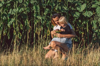 Genç anne bebeğini kucağında tutuyor. Anne ve küçük kızı ayçiçeği tarlasında iyi vakit geçiriyorlar. Anneler Günü. Aile Kavramı