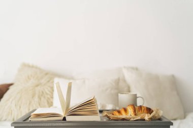 Kruvasan tepsisi, bir fincan kahve ve temiz yatakta kitap. Dikkatli ve sakin bir yaşam..