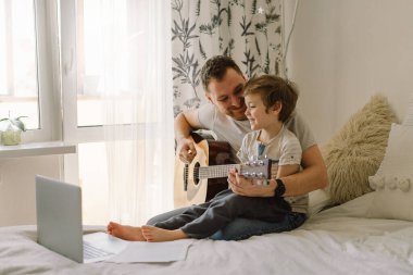 Baba ve oğul online bir derste akustik gitar çalmayı öğrenirler. Oğlumla evde vakit geçirmek, gitar çalmayı öğretmek için. Babalar günün kutlu olsun.