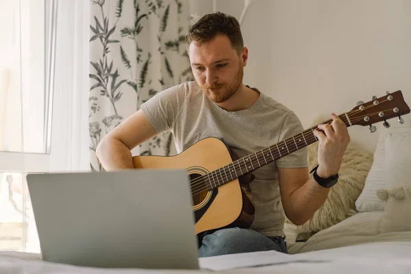 Seorang pria memainkan gitar akustik dalam sebuah pelajaran online. Hobby seorang musisi. — Stok Foto