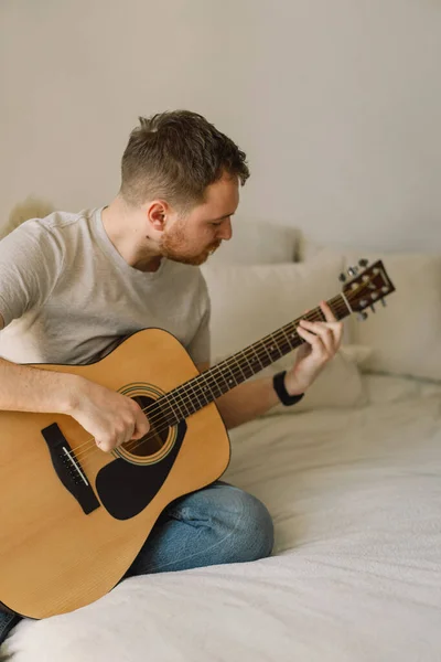 Seorang pria memainkan gitar akustik di sebuah ruangan di rumah. Hobby seorang musisi. — Stok Foto