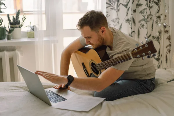 Seorang pria memainkan gitar akustik dalam sebuah pelajaran online. Hobby seorang musisi. — Stok Foto