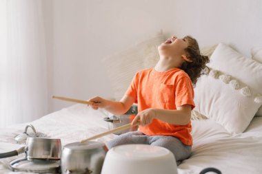 Davul seti gibi yerleştirilmiş tencereleri vurmak için tahta çubuklar kullanan sevimli bir çocuk. Karantina zamanı