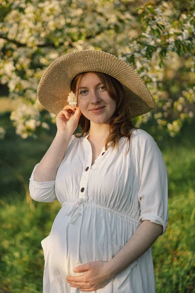 Spring portrait of a pregnant woman. A beautiful young pregnant woman in a white dress walks in the spring garden. Happy pregnancy. Spring