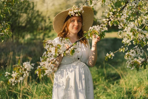 Spring portrait of a pregnant woman. A beautiful young pregnant woman in a white dress walks in the spring garden. Happy pregnancy. Spring