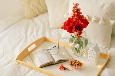 Oturma odasının iç kısımlarında hala hayat detayları var. Açık kitap ve vazo kırmızı laleler. Oku ve dinlen. Sıcak bahar konsepti.