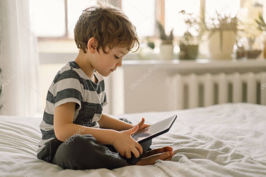 Little Boy with a tablet in the room. The boy play game on the tablet. Technology concept. Child with a gadget