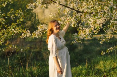 Hamile bir kadının bahar portresi. Beyaz elbiseli güzel hamile bir kadın bahar bahçesinde yürüyor. Mutlu hamilelikler. Bahar