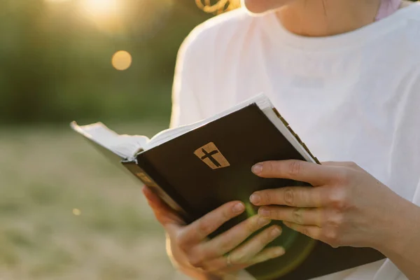 La mujer cristiana tiene la Biblia en sus manos. Leyendo la Santa Biblia en un campo durante el hermoso atardecer. — Foto de Stock
