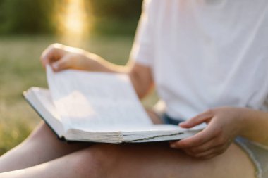 Kadın kitabı elinde tutuyor. Gün batımında bir tarlada kitap okumak..