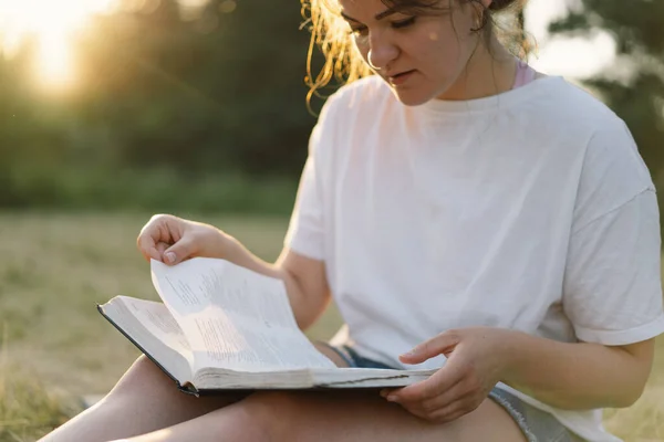 Christelijke vrouw houdt bijbel in haar handen. De Bijbel lezen in een veld tijdens de prachtige zonsondergang. — Stockfoto