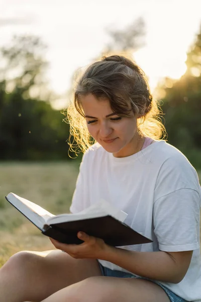 Wanita Kristen memegang Alkitab di tangannya. Membaca Alkitab di lapangan selama matahari terbenam yang indah. — Stok Foto