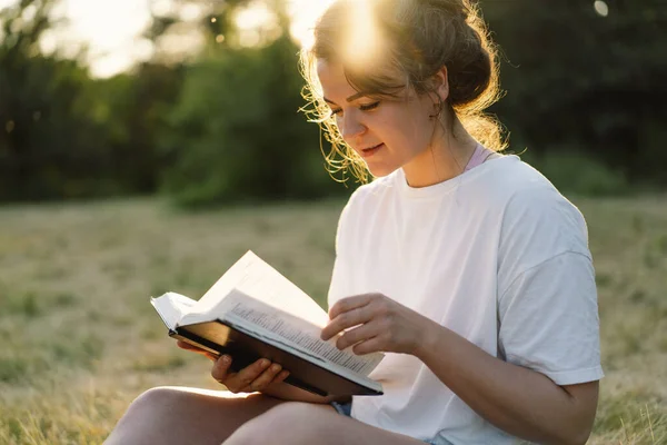 Christelijke vrouw houdt bijbel in haar handen. De Bijbel lezen in een veld tijdens de prachtige zonsondergang. — Stockfoto