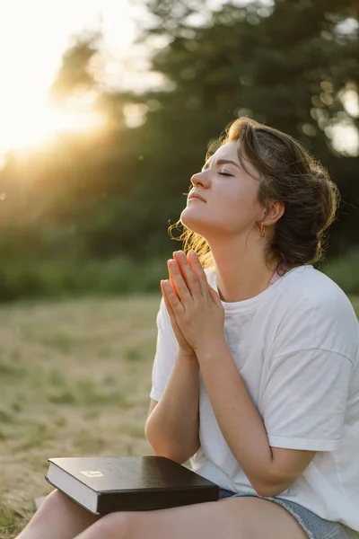 La mujer cerró los ojos, rezando en un campo durante el hermoso atardecer. Manos dobladas en concepto de oración por la fe —  Fotos de Stock