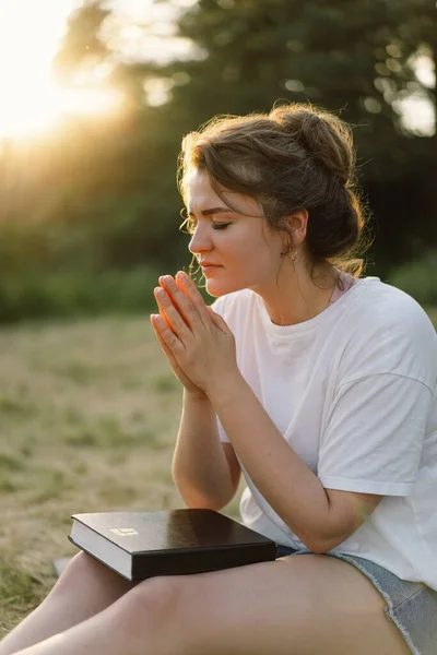 Wanita menutup matanya, berdoa di lapangan saat matahari terbenam yang indah. Tangan dilipat dalam konsep doa untuk iman — Stok Foto