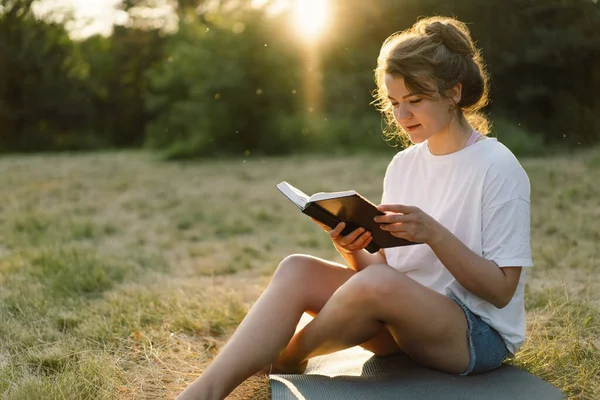 Vrouw houdt boek in haar handen. Het boek lezen in een veld tijdens zonsondergang. — Stockfoto