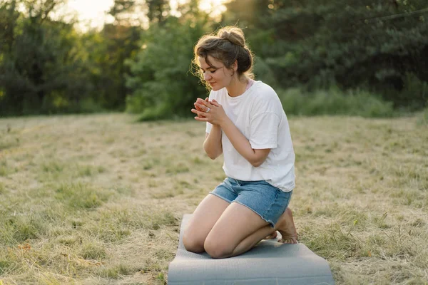 Woman closed her eyes, praying in a field during beautiful sunset. Hands folded in prayer concept for faith — Stock Photo, Image