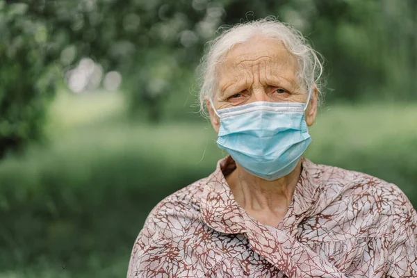 Portrait of a gray-haired sad old woman alone wearing protective face mask while during Covid-19 quarantine. Depressed elder suffering from loneliness during lockdown due to covid.