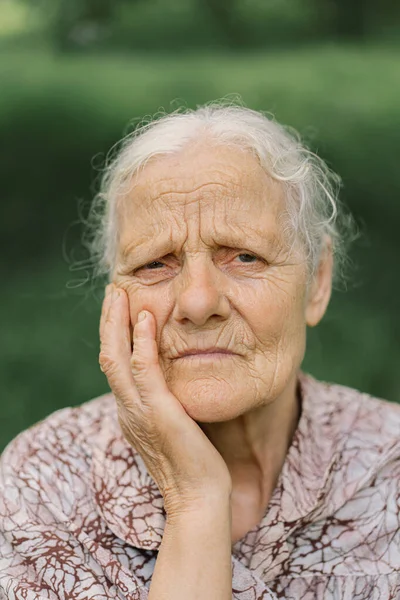 Portrait Sad old woman. Portrait of a gray-haired adult grandmother against the background of nature. Depressed elder suffering from loneliness