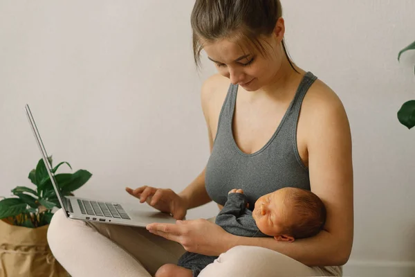 Mother holds her newborn baby son and works at the computer at home. — Stock Photo, Image