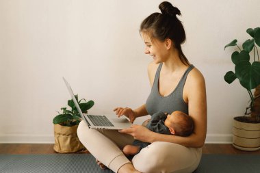 Anne yeni doğmuş bebeğini kucağında tutuyor ve evde bilgisayar başında çalışıyor..